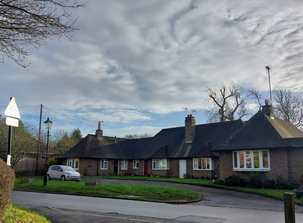 Photo shows a modern complex of joined bungalows against a clouded blue sky
